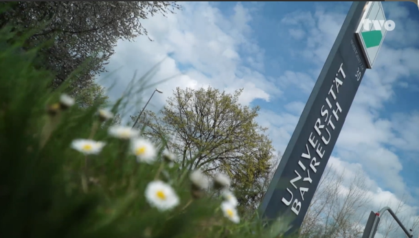 Wiese mit dem Uni Bayreuth Schild im Fokus